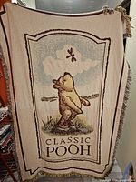 Front side of the throw blanket showing Winnie the Pooh looking up at a dragonfly on a cream background with beige and brown borders.