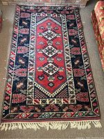 Full view of rectangular area rug placed on carpeted floor with fringed edges and detailed borders