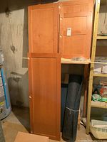 Four wooden cabinet doors stacked vertically and leaning against a wall. Natural medium wood finish, simple paneled design with knobs and hinges attached.