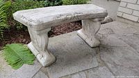 Concrete garden bench showing contoured seat with embossed grapevine and floral designs, with one supporting leg visible in front.