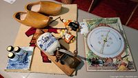 Overview of all items on a table including wooden shoes, Delft coffee grinder, ceramic figurines, metal kitchen decor, and hooked rug.