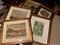 Five framed vintage art prints displayed on a table, showing variety in size and subject