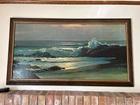 Full front view of wooden framed large print depicting waves crashing on rocky shoreline at sunset or sunrise showing overall framing and condition.