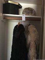 Wide shot showing two fur coats hanging in closet and fur hat with box on shelf