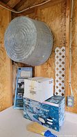 Galvanized metal wash tub hanging on wall above boxes of garden lighting and garden arch kit parts.