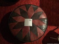 Top view of round leather hassock with geometric star pattern in light and dark brown with a small stain on one brown panel.