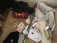 Bags and purses including black, burgundy, and white bags, silver belts, handkerchiefs with various colors, and an art deco umbrella laying on floor.