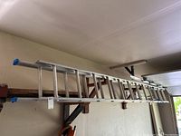 Aluminum extension ladder stored on garage wall, showing whole length with blue rubber caps on both ends.