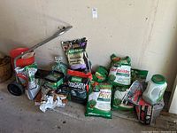 Photo showing push spreader with long handle, several fertilizer and seed bags including Scotts Turf Builder and Golfgreen Nitro Grow, plastic hand spreader.