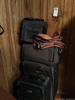 Stack of three Eddie Bauer luggage pieces, brown and black, wheeled with pull handles, plus folded brown/orange duffle and packing cubes on top against wood wall