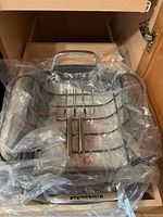 Stainless steel KitchenAid roasting pan with three-pronged metal roasting rack inside, wrapped partially in plastic.