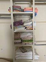 Full shelving rack with folded sheet sets and pillow cases of different colors and patterns on various shelves, white flannel blankets on bottom shelf