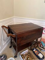 Tea cart from an angle showing wooden construction, drop leafs, and one side with handle and wheels.