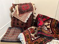 Photo of a stack of small rugs and mats in various ethnic patterns with fringe, stacked one on another