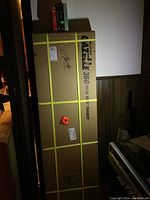 Large cardboard box sealed with yellow straps labeled Tony Little's Gazelle 360 Total Body Trainer with shipping labels and signatures.