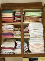 Wooden cabinet shelves filled with assorted folded bath towels and facecloths in various colors and patterns.