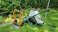 Photo showing both items on grass: the orange adjustable frame dolly cart and the green resin frame wheelbarrow with steel frame and inflated tire.