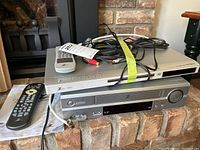 Photo of stacked Zenith DVD player on top of Zenith VCR with remotes and cords placed on DVD player.