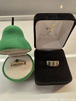 Two rings displayed side by side in open boxes; green suede box for the 10K ring and black eLine Jewelry box for the 14K ring.