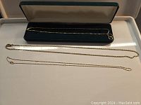 All three necklaces laid out flat beside open green velvet display box on white surface.