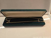 Open green velvet presentation box containing the full length of the gold rope chain laid flat