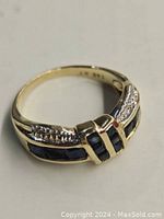 Top view of ring showing channel set square cut blue sapphires flanked by single cut diamonds and 14K hallmark inside band