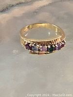 Ring displayed on reflective surface showing arrangement of six gemstones.
