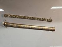 Two gold bracelets displayed on white background, one thin lozenge design and one wide bar link