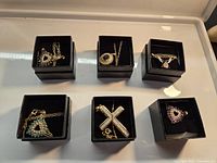 Overview photo showing six black boxes with individual costume necklaces featuring gold-tone chains and various stone pendants.