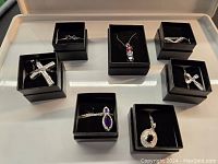 Top down view showing all 7 necklaces, each in a black jewelry box, showcasing variety in pendant shapes and stone colors.