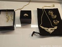 Full view of the assortment of rings, earrings and necklaces displayed in boxes and a black pouch on a white surface.