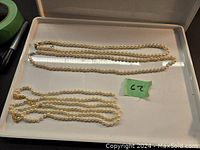 Two faux pearl necklaces laid flat on a tray, showing full length and chain style.