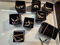 Photo shows all eight necklaces in individual black boxes with gold tone chains and various stones in different colors including purple, deep blue, clear, and red.
