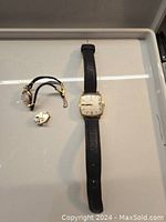 Omega watch, women’s watch case with cord band, and loose movement parts on white tray