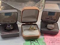 Three sterling silver rings in display boxes, showing amethyst, clear stones, and marcasite detailing.