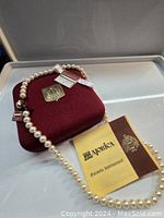Overhead view of red velvet box with Majorica crest, necklace draped over and tag visible.