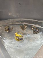 Frontal view of four gold rings on a glass block display