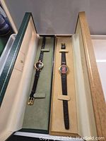 Both watches displayed inside their original hinged presentation boxes, straps laid flat