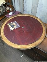 Full view of antique wooden crokinole board, 28 inch round, with wooden playing discs in plastic bag on center surface.