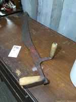 Full view of antique hay saw with curved metal blade and wooden handles on a wooden table.