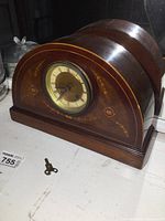 Front view of antique wooden mantel clock with clock face, inlay decoration, and winding key on surface.