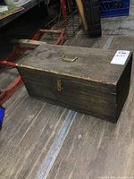 Full side angle view of the antique wooden toolbox showing brass handle and lock on front.