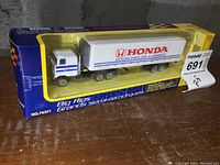 Photo of the Big Rigs Honda tractor trailer toy model in original packaging. Box is mostly blue and yellow with clear display window showing the toy truck inside.