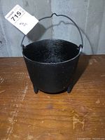 Front view of the black cast iron cauldron showing bowl shape and wire handle upright.