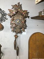 Front view of vintage wooden cuckoo clock showing carved birds, leaves, and two hanging pinecone weights.