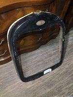 Front view of black painted metal radiator surround with bronze Ford emblem on top center.