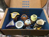 Box containing 7 miniature Toby mugs showing top view with various colored hats and faces visible