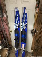 Pair of blue and silver Connelly water skis seen leaning against a door, showing bindings and length.