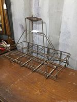 Front angle showing the metal wire construction of the antique oil bottle carrier with a wrapped handle and eight compartments for holding bottles.