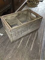 Photo of the vintage wooden Pepsi crate showing side with faded Pepsi Cola stencil and visible aged wooden texture.